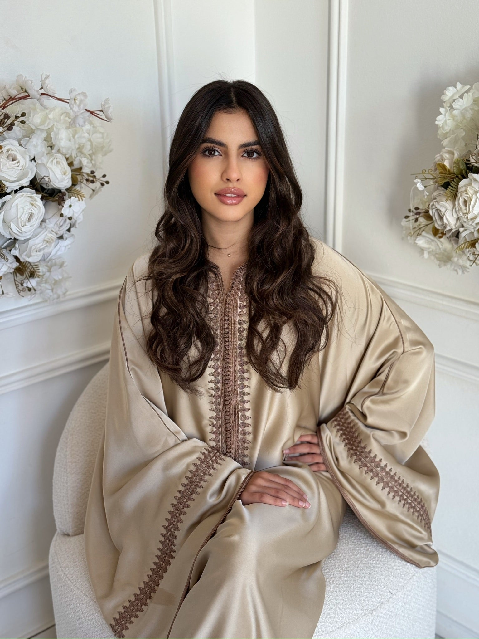 Model wearing a champagne gold Moroccan gandoura in a bright interior with floral décor