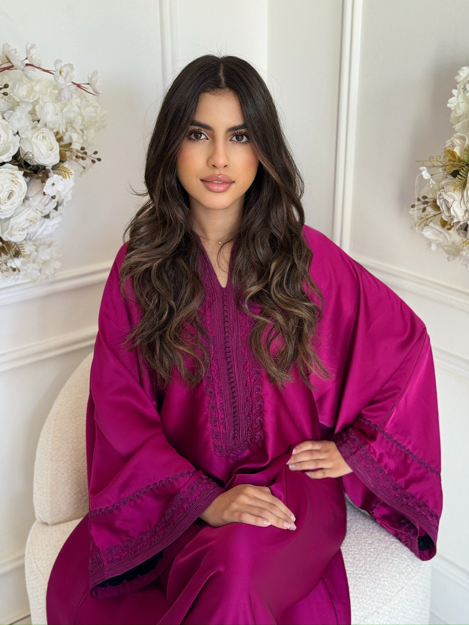 Model wearing a deep rose-pink Moroccan gandoura sitting in a room with white flowers
